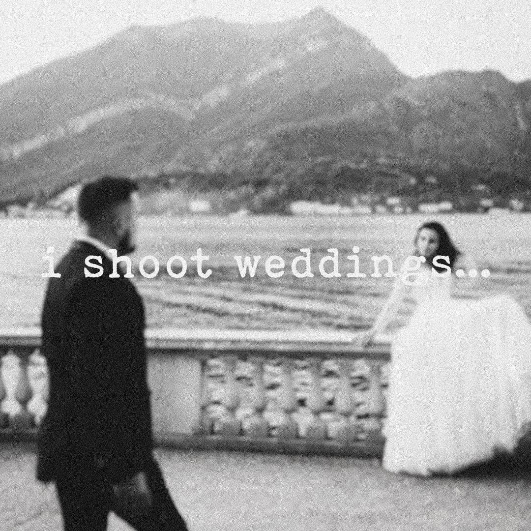 Black-and-white photograph: a groom in the foreground and a bride at a stone balustrade by a lake and mountains, with the words “i shoot weddings…”